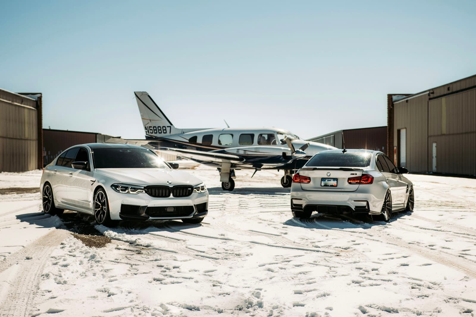Two cars parked on a snowy apron beside a small aircraft