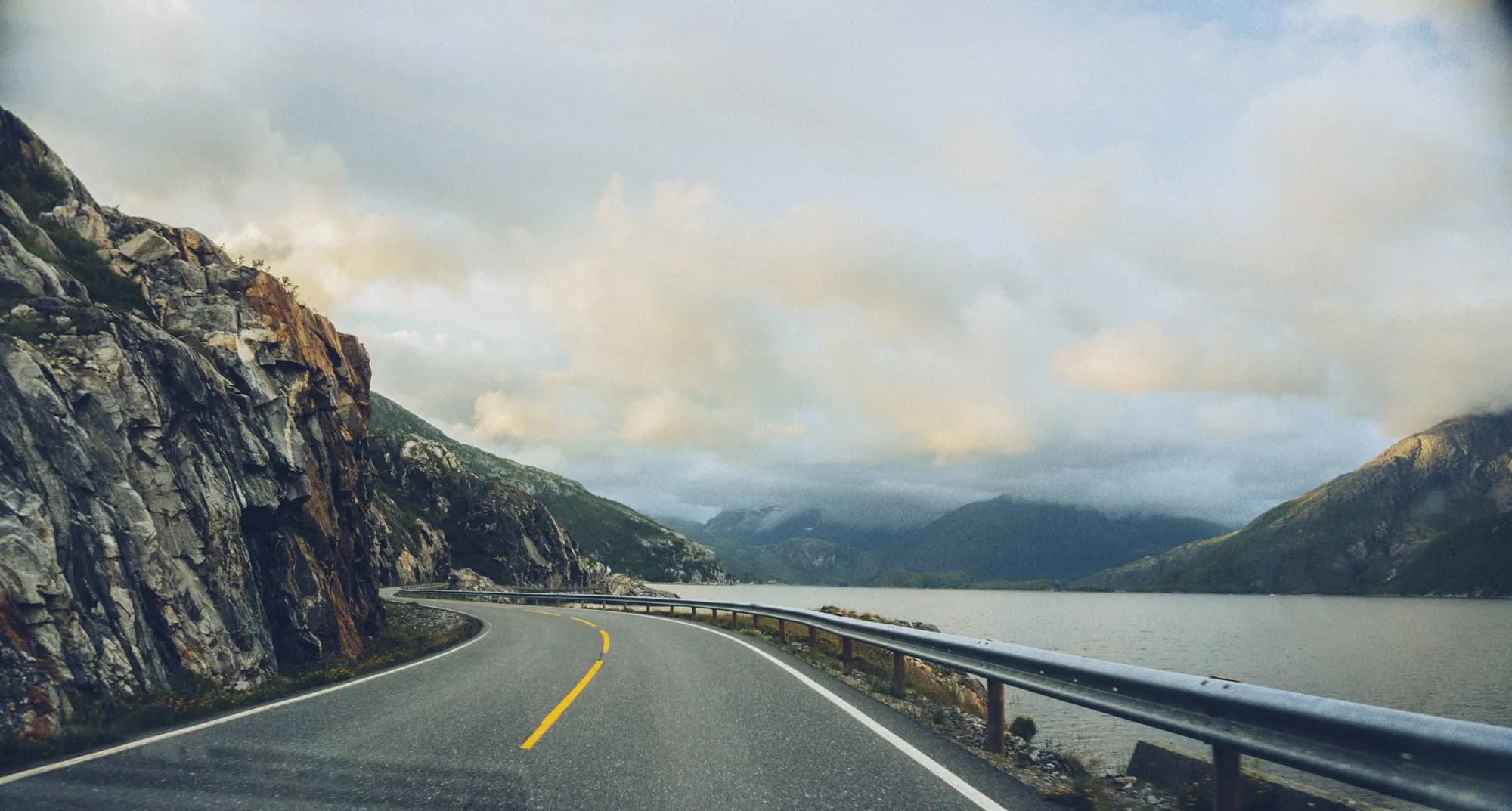 An empty coastal road curving under a rock face along a fjord in Northern Norway