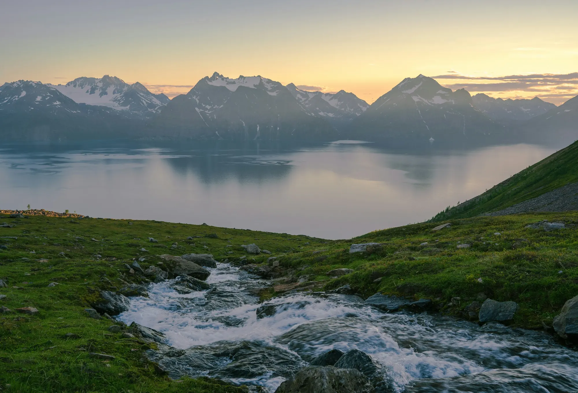 The Lyngen Alps across the fjord from Rotsund on a summer night, a stream running through the grass in the foreground